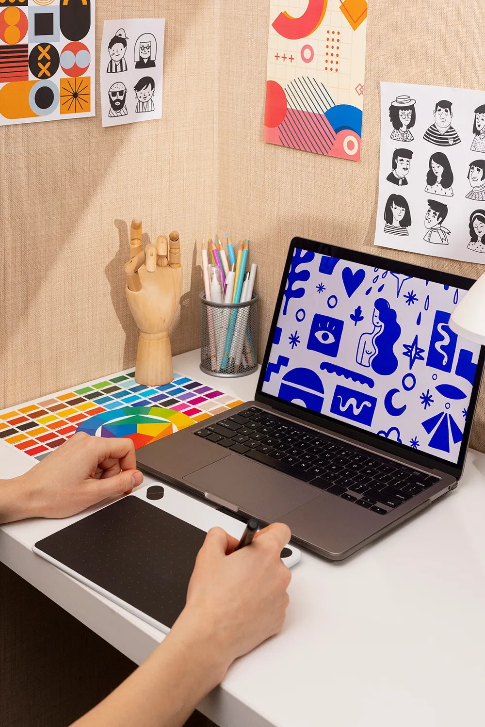 Poste de travail de designer comprenant une tablette graphique, un nuancier de couleurs, un ordinateur affichant des illustrations et des croquis, illustrant le processus de création d’une identité visuelle.