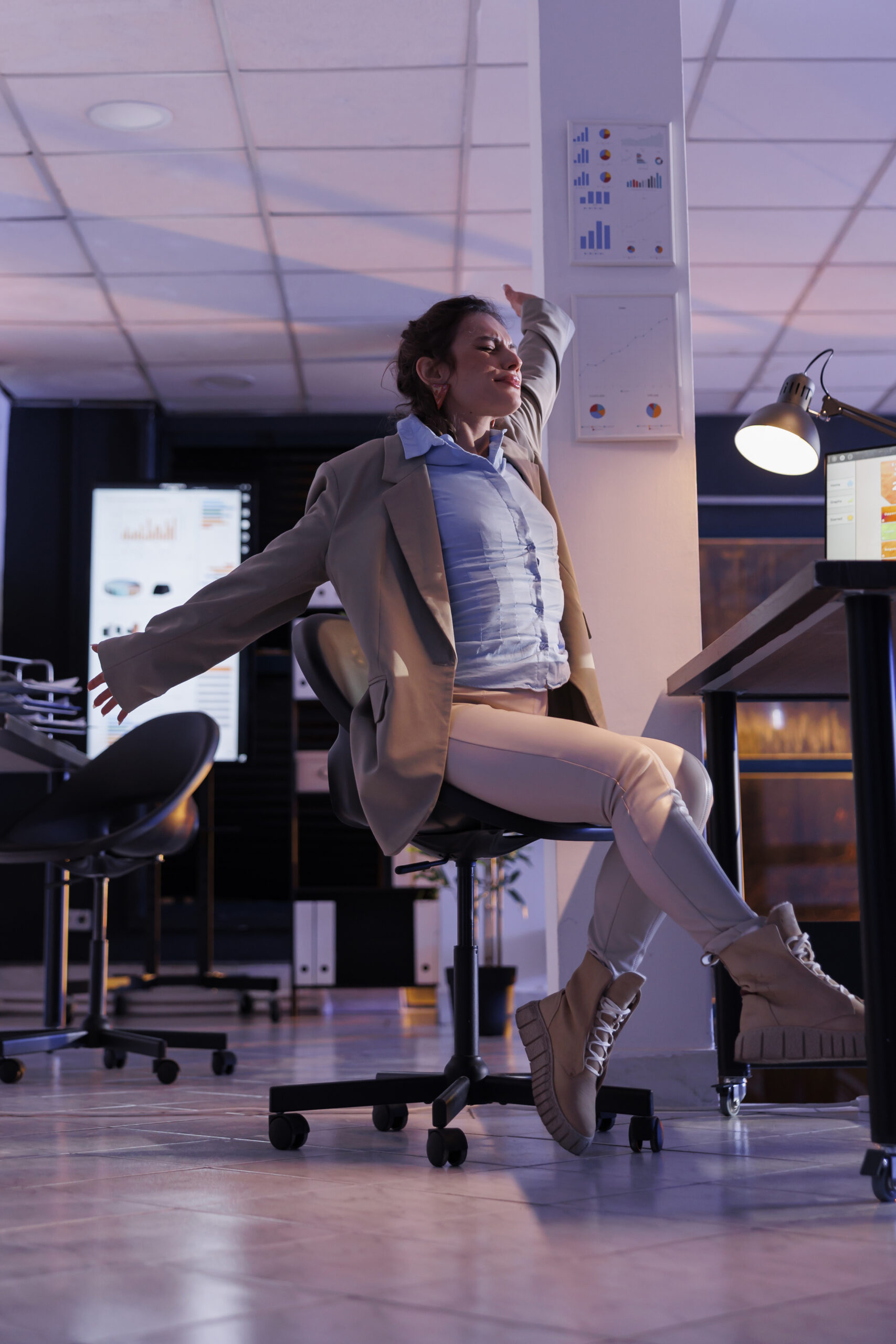 Femme d’affaires s’étirant devant son bureau dans un environnement professionnel moderne, symbolisant la fatigue, la gestion du temps ou le besoin d’organisation.