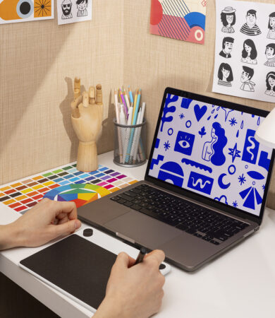 Poste de travail de designer comprenant une tablette graphique, un nuancier de couleurs, un ordinateur affichant des illustrations et des croquis, illustrant le processus de création d’une identité visuelle.